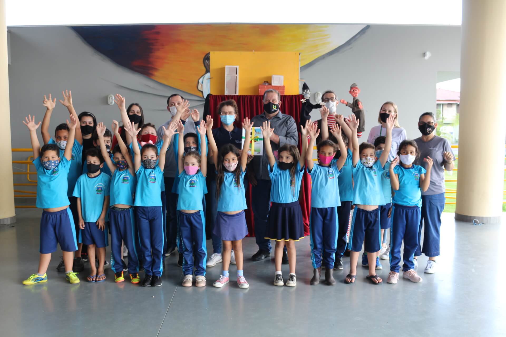 Foto com varias crianças, meninos e meninas, com as mãos para cima, vendo um teatro de fantoches que ensina sobre eficiência energética